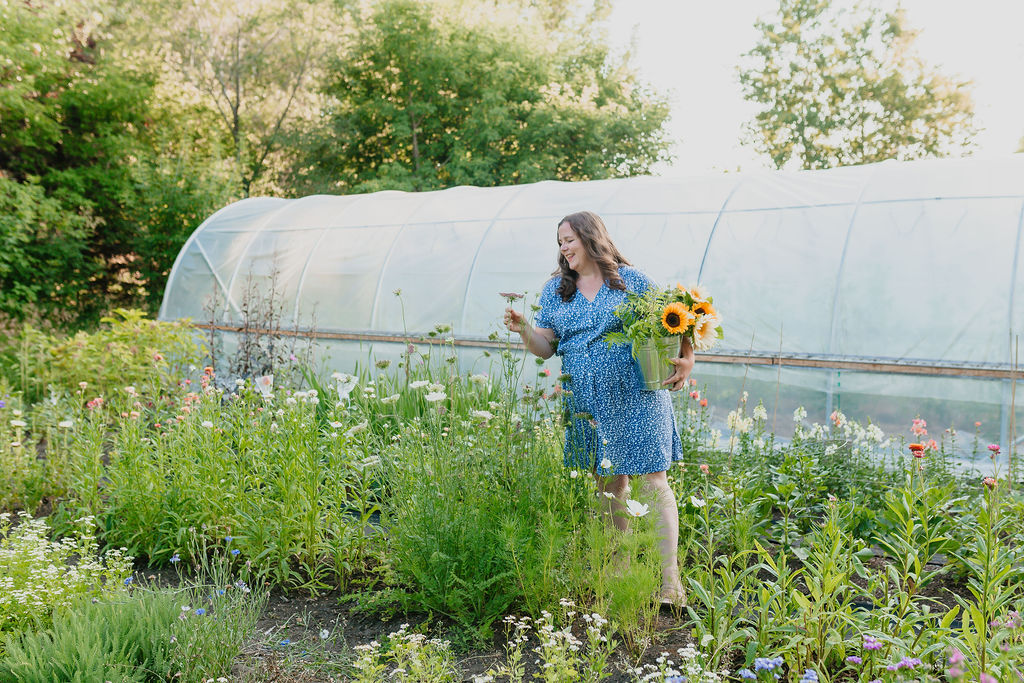 Woman in a blue dress with a bucket of sunflowers in a garden full of cut flowers.