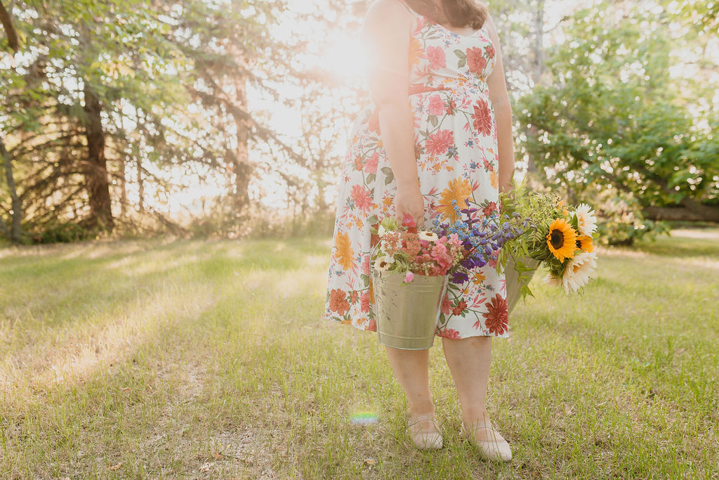 woman in a floral dress holding two buckets of locally cut flowers